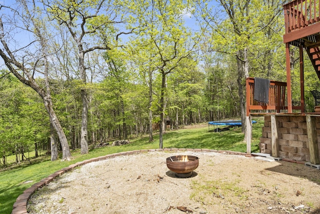 view of yard with a fire pit, a wooden deck, and a trampoline
