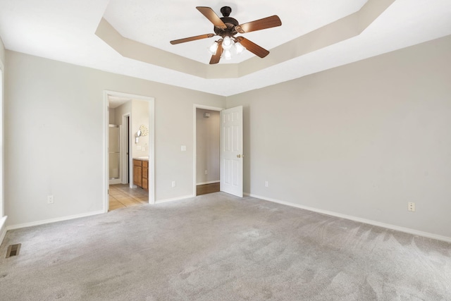 unfurnished bedroom with visible vents, a tray ceiling, baseboards, light carpet, and ensuite bath