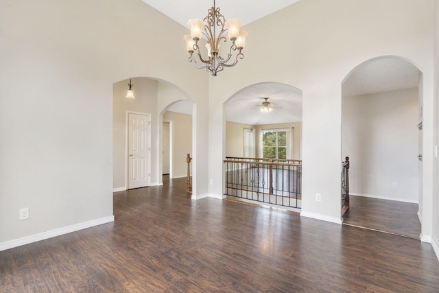 unfurnished room with dark wood-style flooring, a towering ceiling, baseboards, and ceiling fan with notable chandelier
