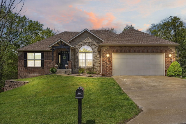 ranch-style home featuring a lawn, driveway, brick siding, roof with shingles, and an attached garage