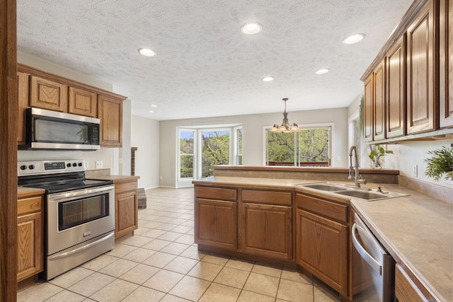 kitchen featuring brown cabinetry, light tile patterned floors, appliances with stainless steel finishes, a sink, and a peninsula