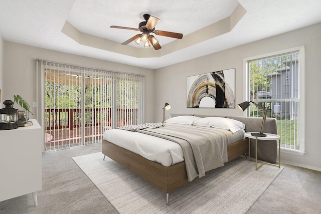 bedroom with carpet flooring, ceiling fan, access to outside, a tray ceiling, and baseboards