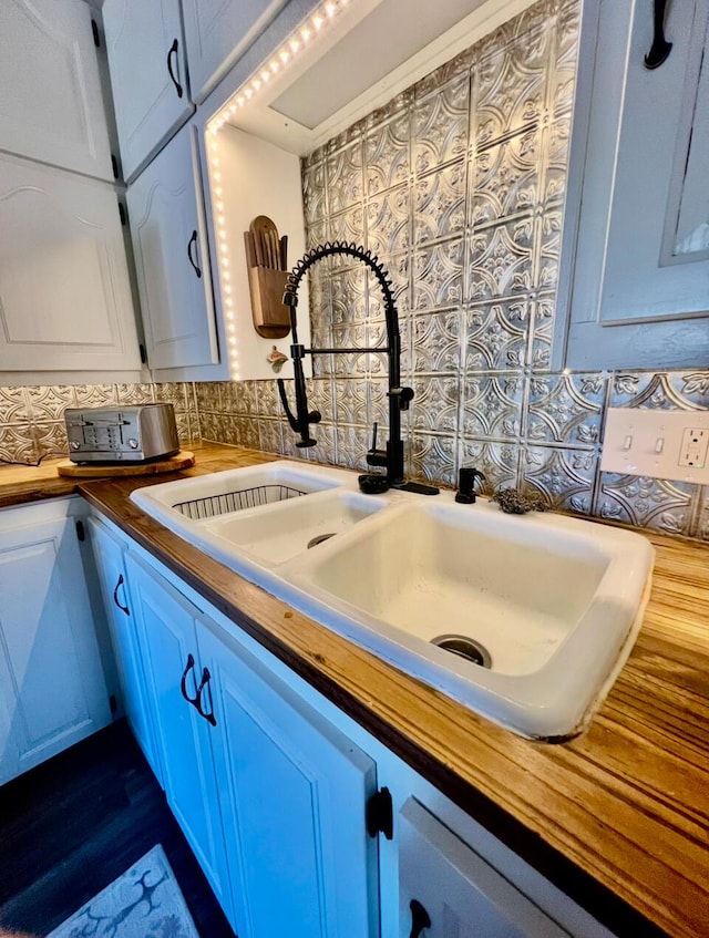 details featuring wooden counters, a sink, backsplash, and white cabinetry