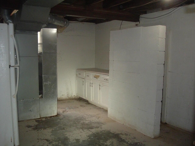 unfinished basement with freestanding refrigerator and concrete block wall