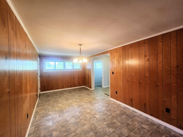 unfurnished dining area with baseboards, a notable chandelier, wooden walls, and stone finish flooring