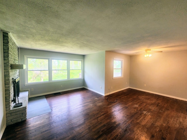 unfurnished living room with a textured ceiling, visible vents, dark wood finished floors, a fireplace, and ceiling fan