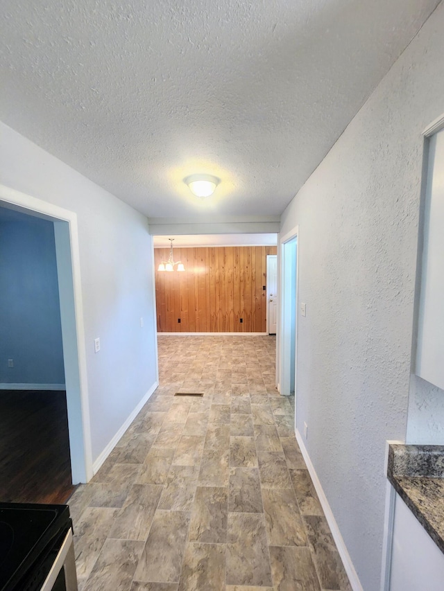 hallway with a textured ceiling, a chandelier, and baseboards