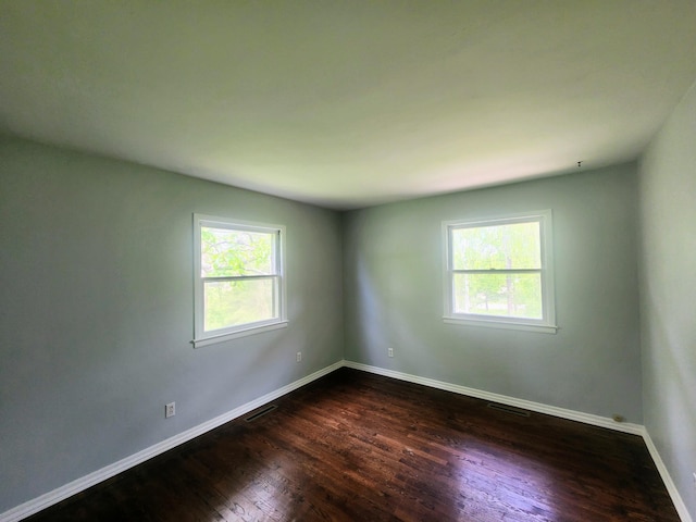 empty room featuring a wealth of natural light, visible vents, dark wood-style flooring, and baseboards