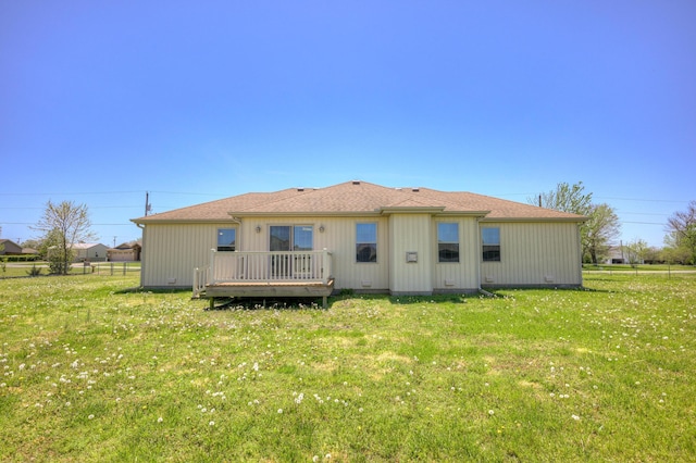 back of property featuring roof with shingles, a yard, and a wooden deck