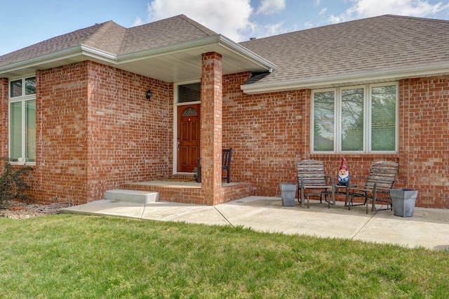 property entrance with brick siding, a lawn, a patio area, and roof with shingles