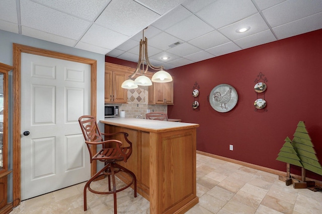kitchen with decorative backsplash, a breakfast bar, stainless steel microwave, visible vents, and a paneled ceiling
