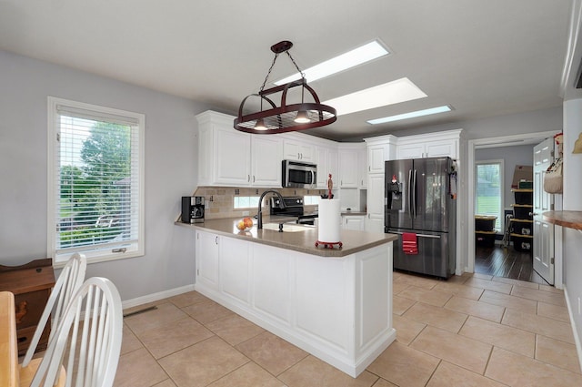 kitchen with a skylight, light tile patterned floors, appliances with stainless steel finishes, a sink, and a peninsula