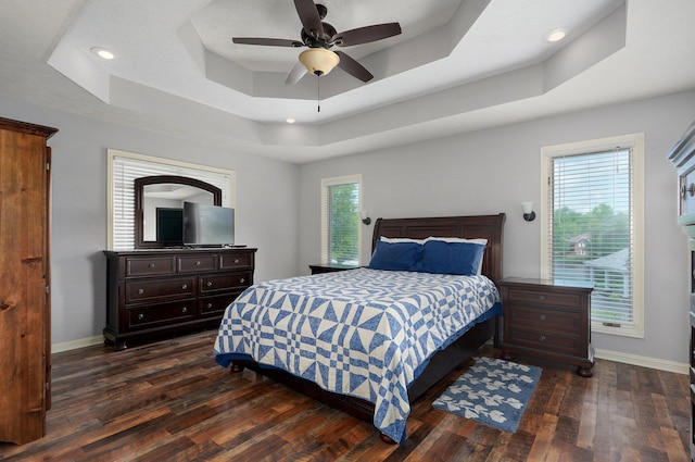 bedroom with dark wood finished floors, baseboards, multiple windows, and a tray ceiling