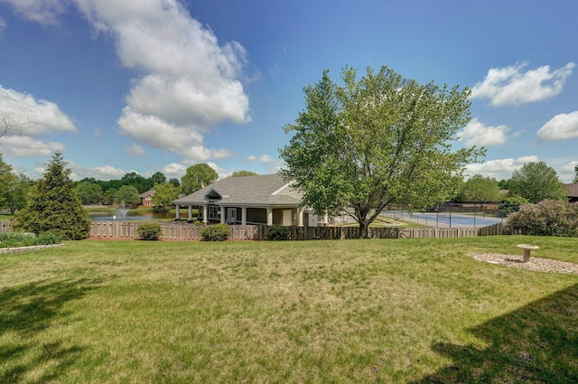 view of yard with fence, a water view, and a tennis court