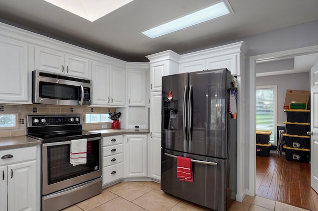 kitchen with light tile patterned floors, white cabinets, backsplash, and stainless steel appliances