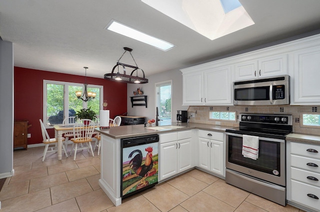 kitchen with white cabinets, a sink, appliances with stainless steel finishes, a peninsula, and a notable chandelier