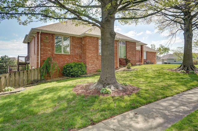 view of property exterior with a lawn, roof with shingles, brick siding, and fence