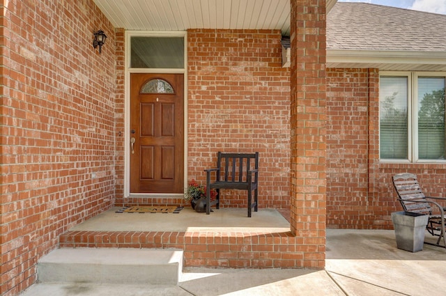 entrance to property with brick siding and a shingled roof