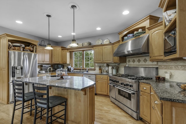 kitchen featuring wall chimney range hood, stainless steel appliances, light wood-type flooring, a kitchen island with sink, and backsplash