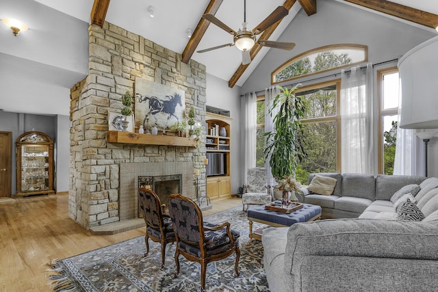 living area with beamed ceiling, ceiling fan, a fireplace, light wood finished floors, and high vaulted ceiling