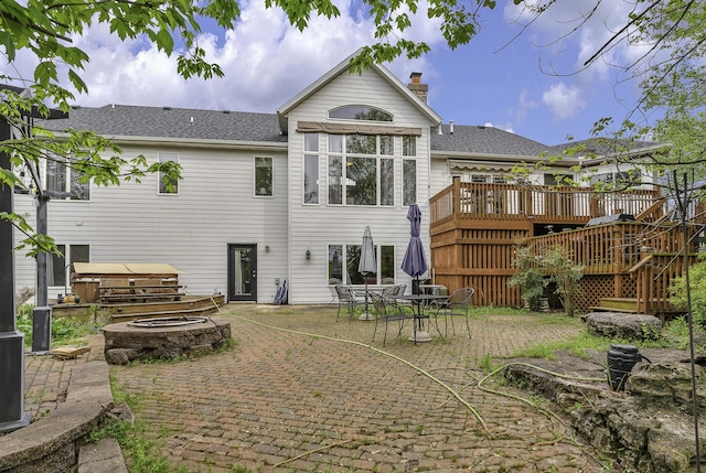 back of house with a patio, a chimney, a wooden deck, and roof with shingles