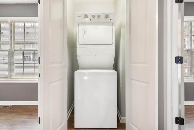 laundry room featuring stacked washer and clothes dryer, wood finished floors, laundry area, and baseboards