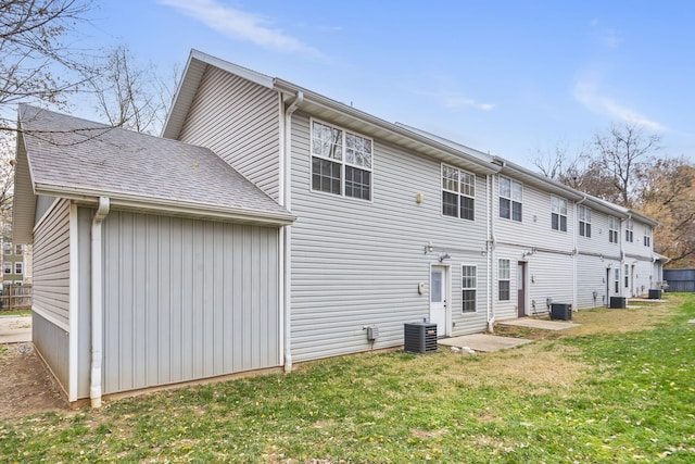 rear view of property with roof with shingles, cooling unit, and a lawn