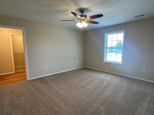 carpeted empty room with a ceiling fan, visible vents, and baseboards