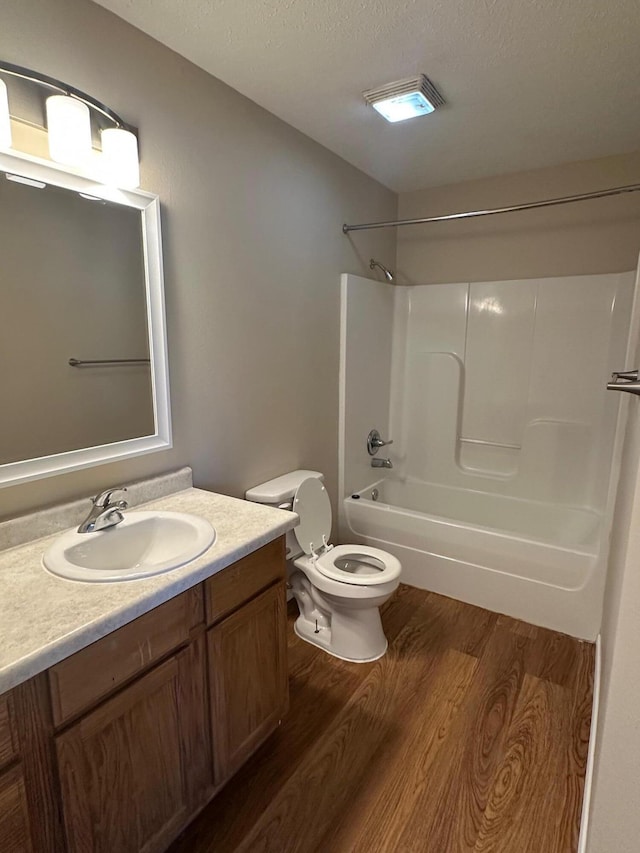 bathroom with wood finished floors, toilet, shower / bathtub combination, vanity, and a textured ceiling