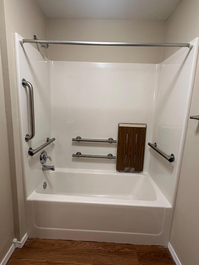 bathroom featuring baseboards, wood finished floors, and shower / bathing tub combination