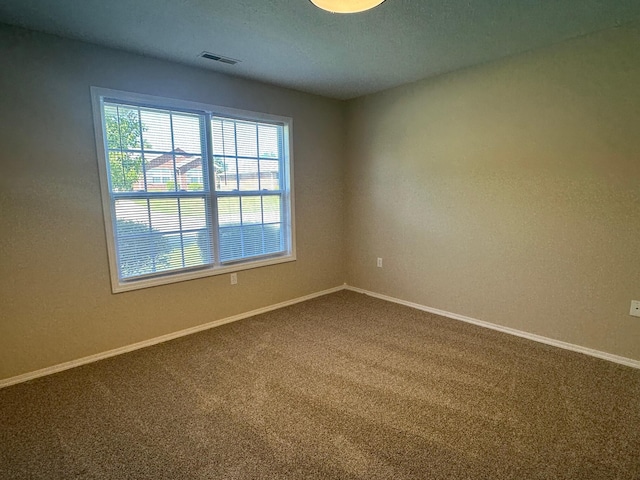 unfurnished room with visible vents, dark carpet, and baseboards