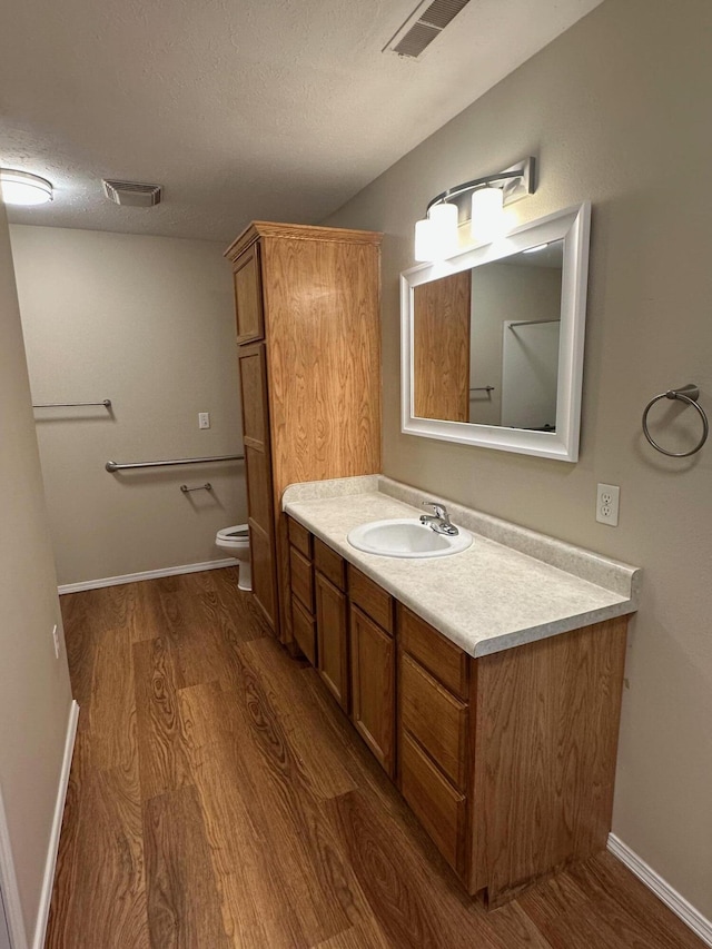 bathroom with toilet, vanity, visible vents, and wood finished floors