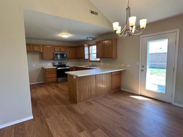 kitchen with brown cabinets, appliances with stainless steel finishes, visible vents, dark wood-style flooring, and a peninsula