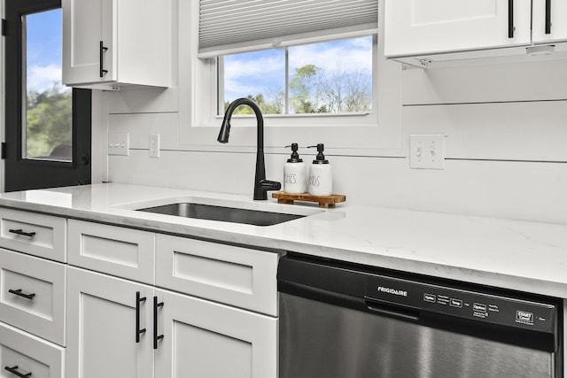 kitchen featuring white cabinetry, stainless steel dishwasher, light stone counters, and a sink