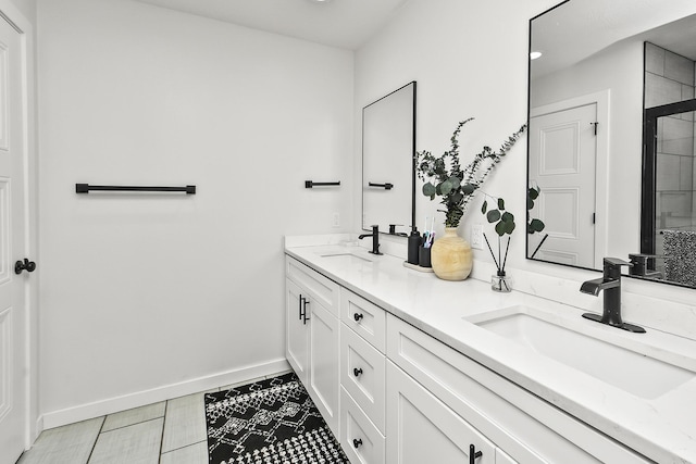 bathroom featuring a tile shower, double vanity, a sink, and baseboards