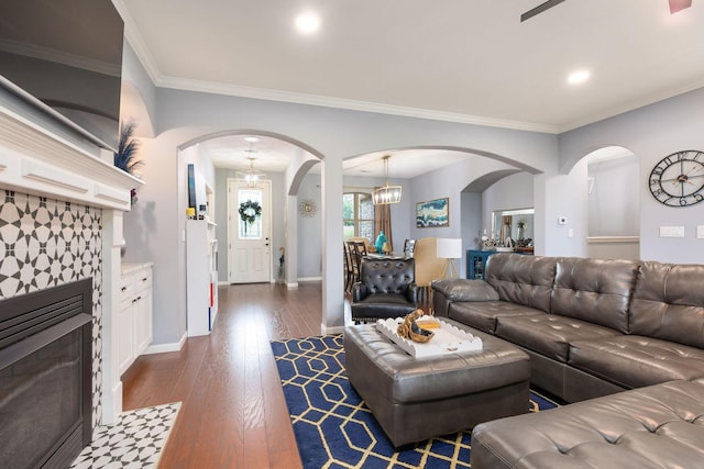 living area featuring dark wood-style floors, a tiled fireplace, baseboards, ornamental molding, and arched walkways