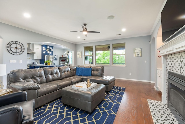 living area featuring ceiling fan, arched walkways, dark wood-style flooring, recessed lighting, and a tiled fireplace