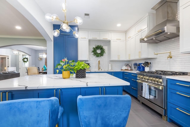 kitchen with wall chimney exhaust hood, high end stove, tasteful backsplash, and blue cabinetry