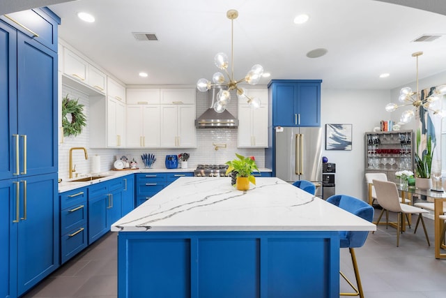 kitchen featuring wall chimney range hood, a sink, visible vents, high end refrigerator, and a notable chandelier