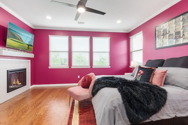 bedroom featuring a tiled fireplace, visible vents, wood finished floors, and crown molding