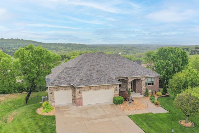 view of front facade featuring driveway, a front yard, an attached garage, fence, and a forest view