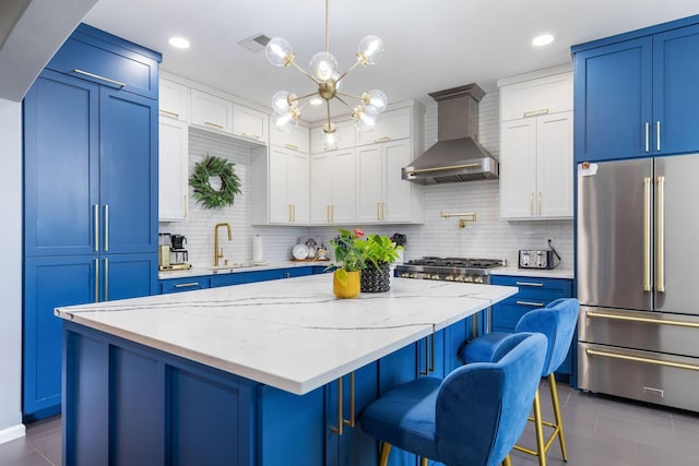 kitchen with stainless steel appliances, blue cabinetry, wall chimney exhaust hood, a kitchen island, and dark tile patterned flooring