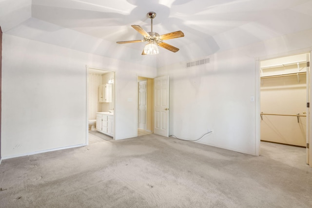 unfurnished bedroom with connected bathroom, light carpet, a walk in closet, visible vents, and lofted ceiling