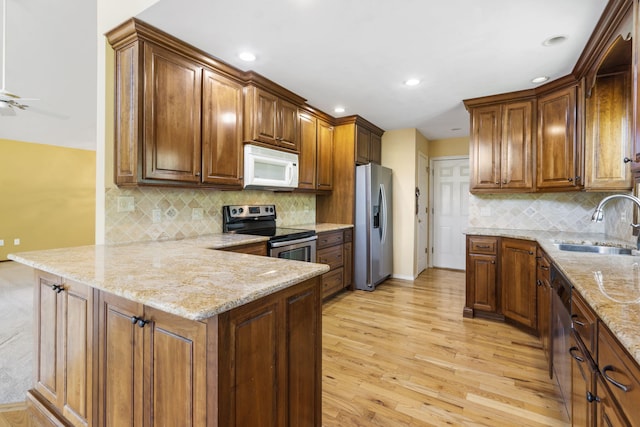 kitchen featuring light stone counters, stainless steel appliances, light wood-style floors, a sink, and a peninsula