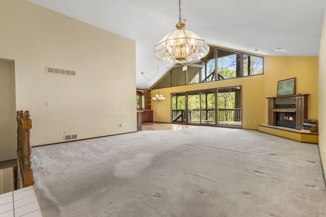 unfurnished living room featuring an inviting chandelier, carpet floors, a warm lit fireplace, visible vents, and high vaulted ceiling