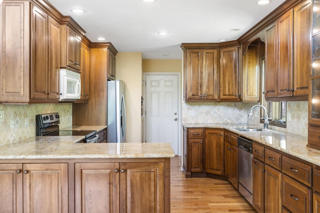 kitchen with light wood-style flooring, light stone counters, stainless steel appliances, backsplash, and a sink