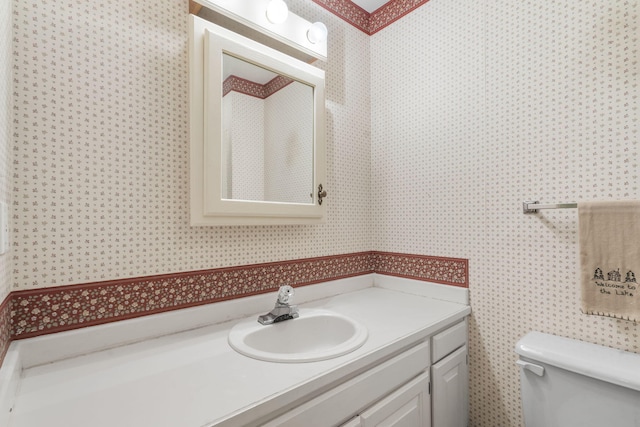half bath with toilet, wallpapered walls, and vanity
