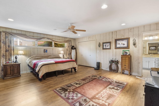 bedroom featuring hardwood / wood-style floors, ensuite bathroom, wooden walls, and a closet