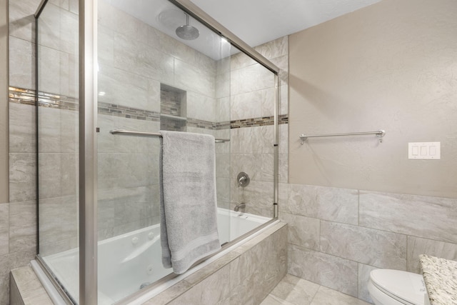 bathroom featuring toilet, a combined bath / shower with rainfall shower, and tile walls