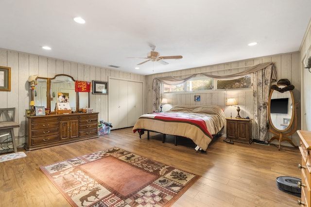 bedroom featuring wood walls, hardwood / wood-style floors, a closet, recessed lighting, and a ceiling fan
